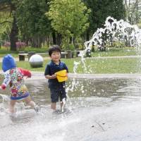 Children play in a water fountain at a park in Asahikawa, Hokkaido, on Friday. Some parts of the prefecture saw the mercury rise above 30 degrees, with the temperature in Asahikawa hitting 26, prompting the Meteorological Agency to issue its first hot weather and heat stroke warnings of the summer. | KYODO