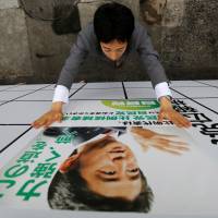 An LDP staff member puts up a poster for the July 10 Upper House election featuring Prime Minister Shinzo Abe at the party\'s headquarters in Tokyo on Wednesday. The slogan on the poster reads: \"Moving forward with strength.\" | REUTERS