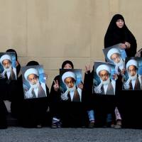 Bahraini anti-government protesters hold posters of top Shiite cleric Sheik Isa Qassim as they wait for a demonstration in Karrana, Bahrain, in May 2013. | AP