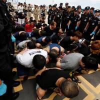 Wire fraud suspects are surrounded by police at Phnom Penh airport before being deported to China on Friday. | REUTERS