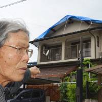 Kumamoto resident Manabu Iwasaki points to his damaged home, whose roof tiles were damaged by the April 14 major earthquake. | KYODO
