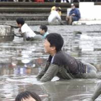 Children swim in mud Sunday as part of the Kashima Gatalympic sports festival held on the mud flats by the Ariake Sea in Kashima, Saga Prefecture. About 1,200 people from Japan and abroad participated in the annual event, which is aimed at promoting the versatility and environment of the flats. | KYODO
