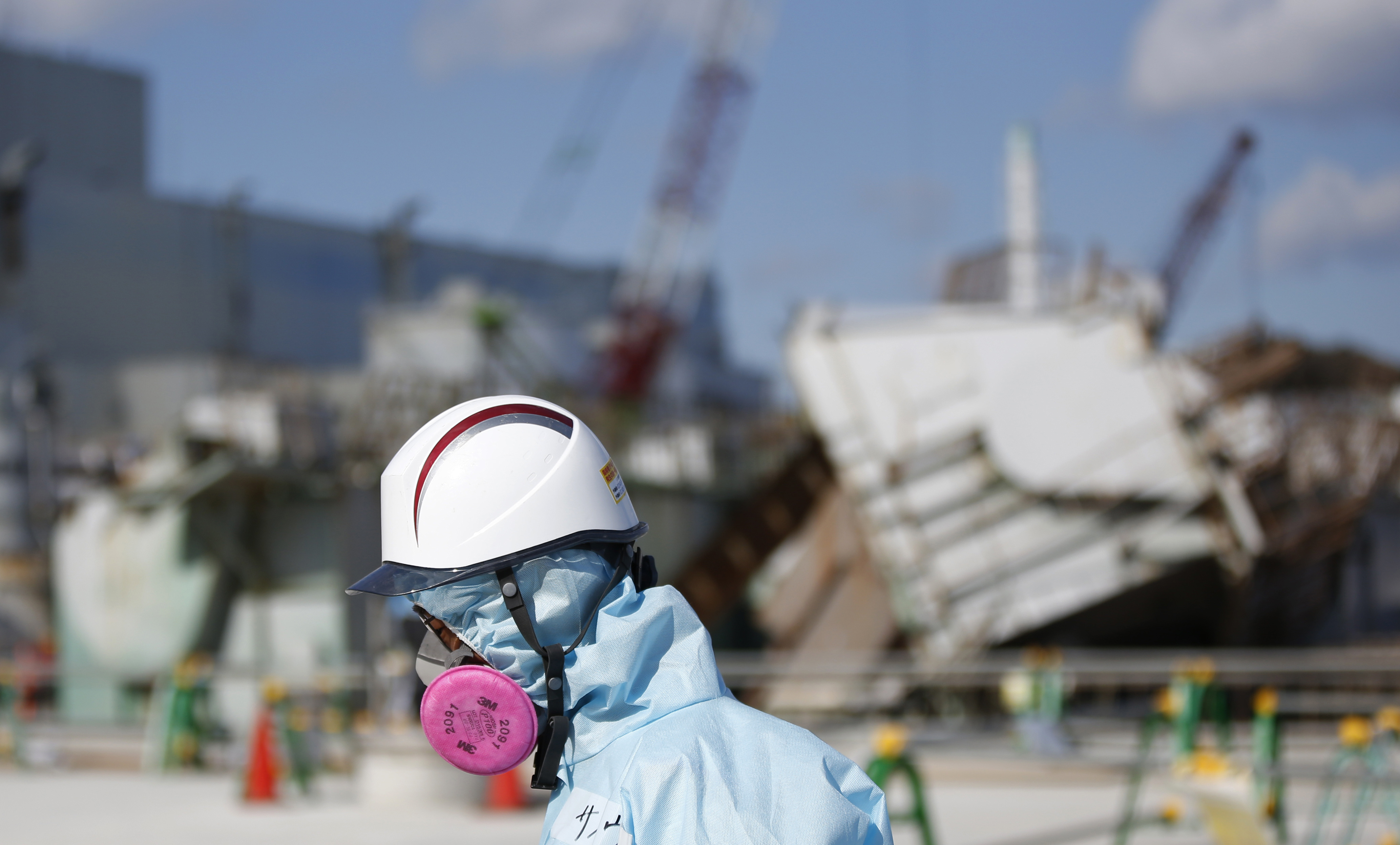 A Tokyo Electric employee in protective gear walks in front of the No. 1 reactor building at the Fukushima No. 1 nuclear power plant in the town of Okuma, Fukushima Prefecture, on Feb. 10. | BLOOMBERG
