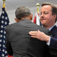 British Prime Minister David Cameron hugs U.S. President Barack Obama after a NATO summit meeting in Warsaw on Saturday. | AFP-JIJI