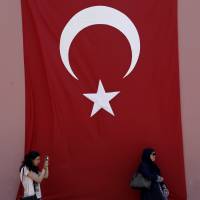 A woman takes photos as an another stands by a Turkish flag in the historic Sultanahmet district of Istanbul on Tuesday. | AP