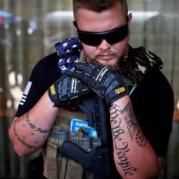 West Ohio Minutemen member Trevor Leis, whose tattoos include the words \"We the People\" from the Constitution, rests on his assault rifle while taking a break from patrolling downtown Cleveland during the Republican National Convention on Tuesday. | REUTERS