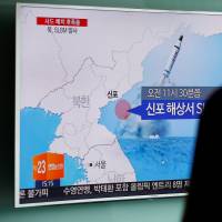 A woman walks past a TV screen at a railway station in Seoul broadcasting a news report on a North Korean submarine-launched ballistic missile test on July 9. | REUTERS