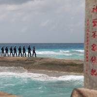 Chinese People\'s Liberation Army Navy personnel patrol in the Spratly Islands, known in China as the Nansha Islands, in February. The sign reads \"Nansha is our national land, sacred and inviolable.\" | REUTERS
