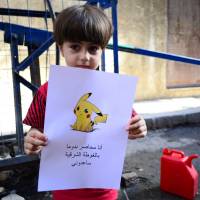 In this handout photo a Syrian boy is seen holding a picture depicting a Pokemon character. The banner reads, \"I am trapped in Douma in Eastern Ghouta. Help me.\" | REUTERS