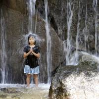 A girl stands under a waterfall like a meditating Buddhist monk in the water fountain at Asuka Park in Tokyo amid high temperatures Monday. | AP