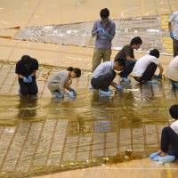 JAXA workers and others attach electric wiring to a thin film that contains solar panels on July 13 in Sagamihara, Kanagawa Prefecture. | SATOKO KAWASAKI
