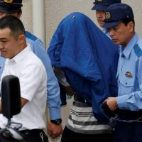 State of shock: Satoshi Uematsu (center, with a jacket over his head), who allegedly murdered 19 residents at a facility for people with disabilities, is escorted by police officers as he is taken from Tsukui police station in Sagamihara, Kanagawa Prefecture. | ISSEI KATO / REUTERS
