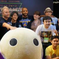 In the game: James Mielke (reaching out to the mascot) and John Davis (second to the right of Mielke) join other members of the BitSummit team for a group photo with some of this year\'s BitSummit Award winner. | JASON COSKREY