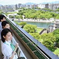 People look over Hiroshima’s Atomic Bomb Dome and Peace Memorial Park from the observation deck of Orizuru Tower on Wednesday. The new 14-floor office and commercial complex has a glass wall that will contain up to 1 million paper cranes. | KYODO