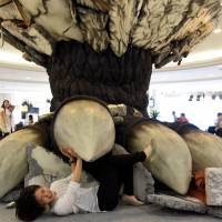 A woman lies under a mock Godzilla foot set up at the Namja Town amusement park in Tokyo\'s Ikebukuro district on Tuesday. The gigantic foot is on display ahead of the release of the \"Godzilla Resurgence\" movie on July 29. | SATOKO KAWASAKI