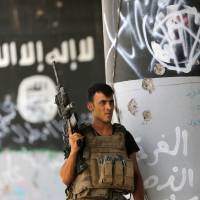 A member of Iraq\'s counterterrorism forces stands guard near Islamic State group graffiti in Fallujah, Iraq, on June 27. | AP