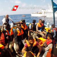 This image grab taken from a handout video and released by the Italian coast guard (Guardia Costiera) on Tuesday shows Italian coast guard personnel taking part in a rescue operation of a boat with migrants in the Mediterranean Sea. | GUARDIA COSTIERA / HO / AFP-JIJI