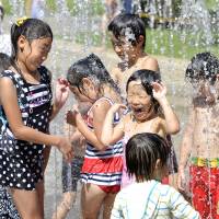 Children play in water at a park in Tokyo on Friday, the day the mercury climbed to 35.0 C or above at 77 observation points out of the 929 across the nation. | KYODO