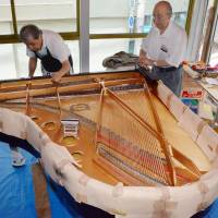 Teruo Inoue (right) oversees repairs to a grand piano damaged by the March 2011 tsunami that will be donated to a hospital in Ishinomaki, Miyagi Prefecture, at his shop in the city last month. | KYODO