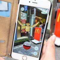 A woman plays Nintendo\'s \'Pokemon Go\' game on her smartphone in front of a McDonald\'s restaurant in Tokyo\'s Akihabara shopping district. | AFP-JIJI