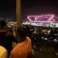 People watch fireworks explode over the Maracana Stadium from the roof of their home in the Mangueira favela, or slum, as the Olympic Opening Ceremony unfolds. | REUTERS