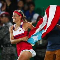 Monica Puig celebrates with a Puerto Rican flag after winning the women\'s singles tennis final at the 2016 Rio Olympics on Saturday. It was the first-ever Olympic gold medal for Puerto Rico. | KYODO