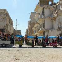 Children ride in carts near damaged buildings during the third day of Eid al-Adha in the rebel controlled city of Idlib, Syria, Wednesday. | REUTERS