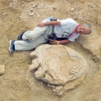 Shinobu Ishigaki, a professor at Okayama University of Science, poses besides a fossilized cast of a dinosaur footprint in Mongolia\'s Gobi Desert on Aug. 21. | KYODO