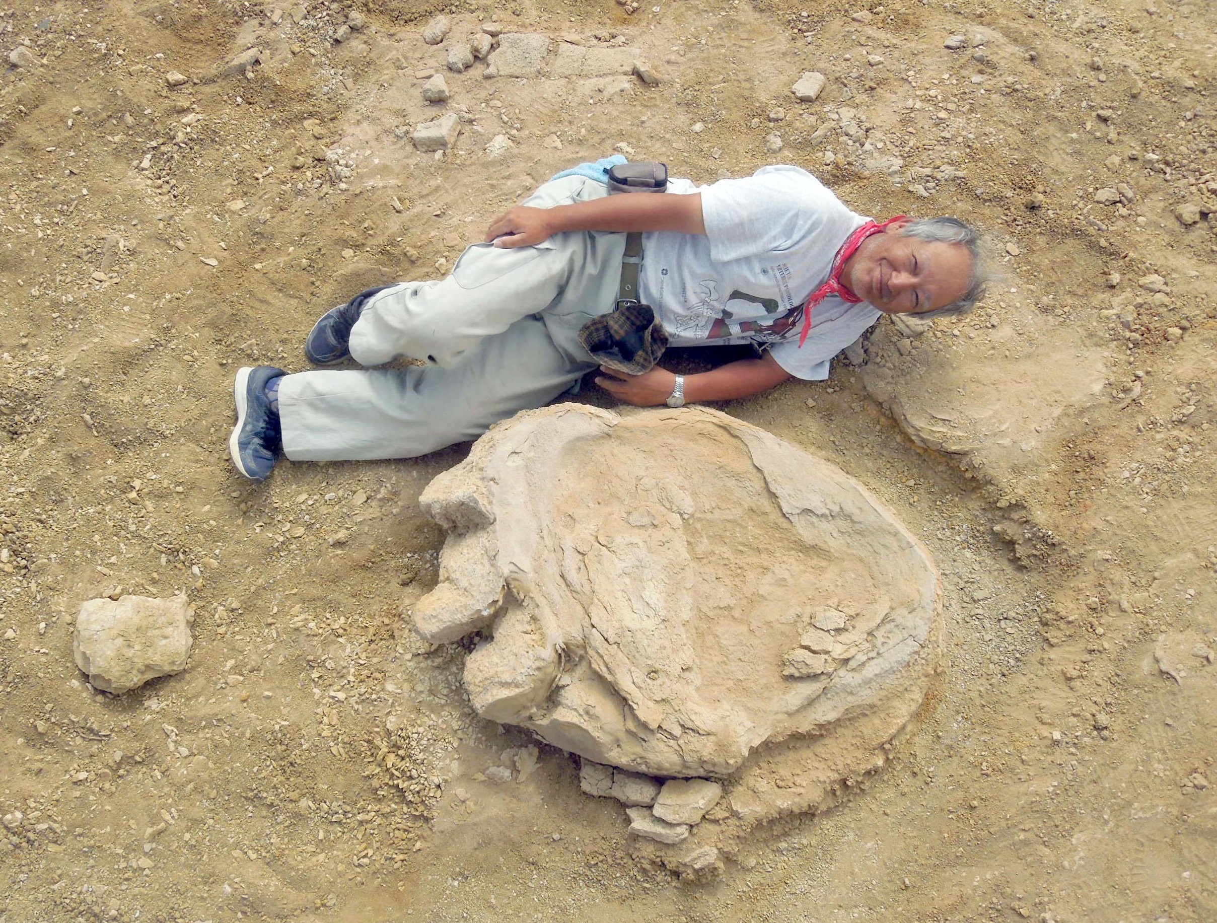 Shinobu Ishigaki, a professor at Okayama University of Science, poses besides a fossilized cast of a dinosaur footprint in Mongolia's Gobi Desert on Aug. 21. | KYODO