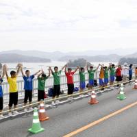 Participants taking part in a pinky swearing event held in the Amakusa area of Kumamoto Prefecture on Sunday raise their arms with their little fingers entwined. | KYODO