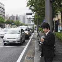 Technological limitations: A businessman sends a text message while waiting to cross a street in Kyoto.  | ISTOCK