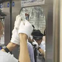 A railway official removes broken glass from the door of a Denentoshi Line train in Setagaya Ward, Tokyo, on Friday after a high school student accidentally shattered it with his head when the packed rush hour train started swaying at around 7:45 a.m. The teenager sustained minor injuries and is recovering. | TOKYU CORP. / VIA KYODO
