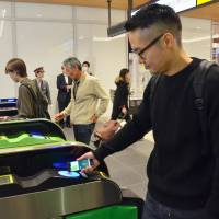 A man uses Apple Pay on his smartphone to get through a ticket gate at JR Shinjuku Station on Tuesday. The service began in Japan the same day. | KYODO