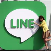 A woman poses next to Line Corp. signage as a man takes a photo in Urayasu, Chiba Prefecture, in 2014. | BLOOMBERG