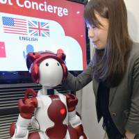 A woman pats Emiew3, a humanoid robot that serves tourists in English, Chinese and Japanese, at JR Tokyo Station, on Monday. | KYODO