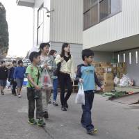 Students on their way to class Monday pass by a school gym that is being used as a quake evacuation center in Kurayoshi, Tottori Prefecture. | KYODO