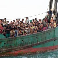Migrants from Myanmar, including Rohingya Muslims, sit in a boat as they wait to be rescued by Aceh fishermen in the sea off Indonesia in May 2015. | AP