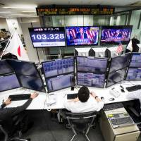 Japanese employees of a foreign exchange trading company work in Tokyo on Wednesday, as U.S. President-elect Donald Trump is seen on television screens delivering his victory speech. | AFP-JIJI