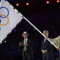 Tokyo Gov. Yuriko Koike waves the Olympic flag as Rio de Janeiro Mayor Eduardo Paes (left) and IOC President Thomas Bach watch during the 2016 Summer Olympics closing ceremony in late August.  | AP