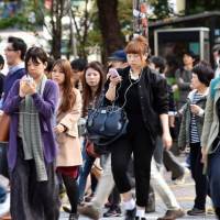 Smartphone in hand, pedestrians cross a busy Tokyo street on Nov. 3. | AFP-JIJI