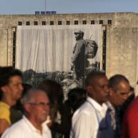 A large portrait of Cuba\'s late President Fidel Castro hangs from a building while people wait in line to pay tribute to Castro in Havana Monday. | REUTERS