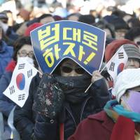 A supporter of South Korean President Park Geun-hye holds national flags during a rally opposing her resignation in Seoul on Thursday. | AP