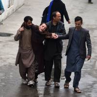Afghan men assist a woman, who collapsed after a massive suicide blast at a Shiite mosque, to the Estiqlal Hospital in Kabul on Monday. | AFP-JIJI