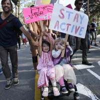 Two girls hold up signs while riding in a stroller during an anti-Trump march through San Francisco\'s Golden Gate Park on Sunday. | AP