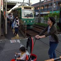 A mother pushes a baby cart across streetcar tracks in Tokyo\'s Arakawa Ward on Oct. 20. | SATOKO KAWASAKI