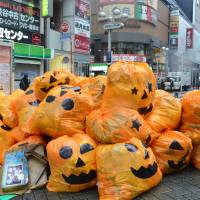 Jack-o\'-lantern plastic bags filled with trash left by costumed partygoers are piled up on a sidewalk in Shibuya Ward, Tokyo, early Tuesday. | KYODO