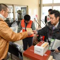 A resident (left) receives iodine tablets while taking part in a disaster drill Monday in Kyowa, Hokkaido. | KYODO