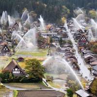 The famed thatched-roof houses in the village of Shirakawa, Gifu Prefecture, are hosed down Sunday as part of its annual fire drill. Firefighters used 59 water cannons to drench the 114 historic houses at the UNESCO World Heritage site. | KYODO