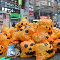 Jack-o\'-lantern plastic bags filled with trash left by costumed partygoers are piled up on a sidewalk in Shibuya Ward, Tokyo, early Tuesday. More than 1,700 volunteers joined the cleanup effort between Friday and Tuesday morning. | KYODO
