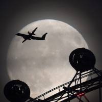 An airplane flies past the London Eye Ferris wheel as the moon looms behind on Sunday. The brightest moon in almost 69 years will be lighting up the sky this week in a treat for sky watchers around the globe. The phenomenon, known as the supermoon, won\'t appear this big and bright again for another 18 years. | REUTERS